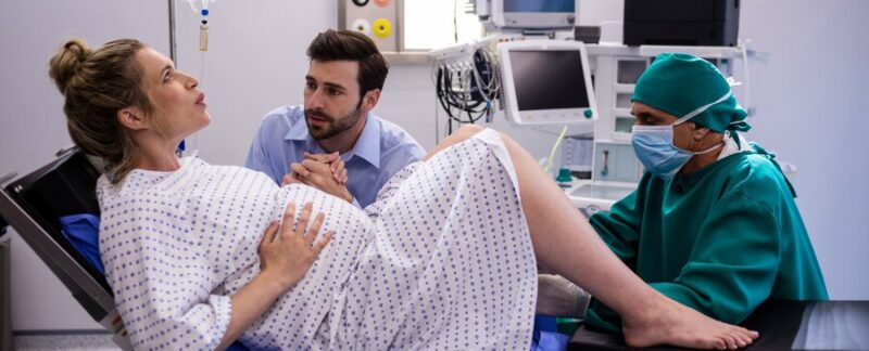 Médecin examinant une femme enceinte pendant l'accouchement, tandis qu'un homme lui tient la main. meilleurs centres de fécondation assistée en France