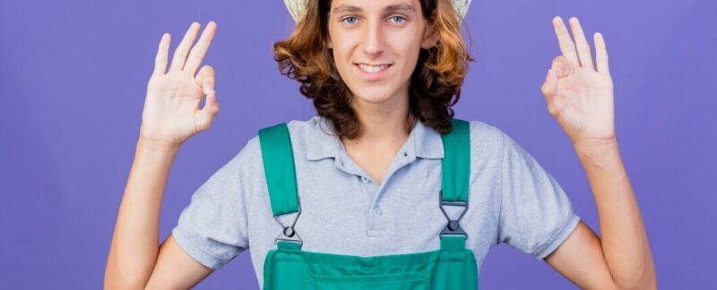 Jeune jardinier vêtu d'une salopette et d'un chapeau, souriant et montrant le signe « ok ». Les meilleures pépinières de France