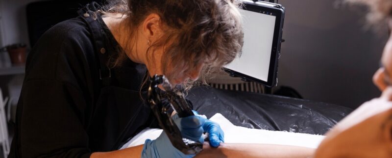 Vue latérale d'un tatoueur en train de faire son travail. meilleurs centres de détatouage en France