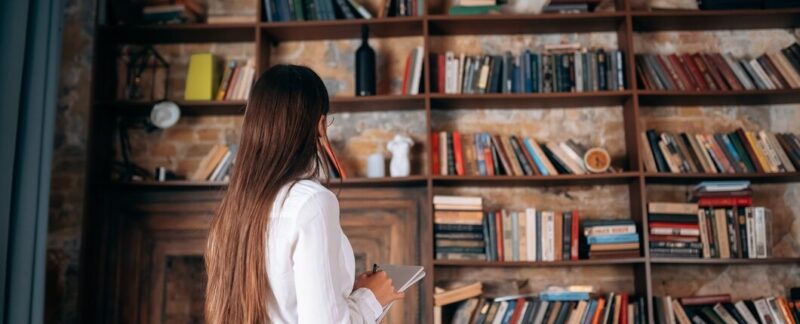 Belle jeune femme à lunettes tenant un carnet de notes et regardant l'étagère. bibliothèques en France