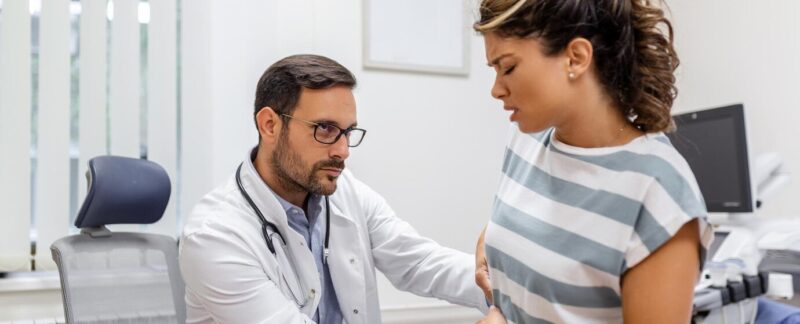 Patient parlant au médecin de sa douleur et de ses problèmes de santé lors d'une visite à l'hôpital Jeune femme se plaignant de douleurs au dos ou aux reins, assise sur la table d'examen dans le cabinet du médecin. meilleurs médecins spécialistes de l'appareil digestif