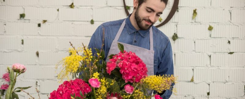 Portrait d'un fleuriste masculin arrangeant des fleurs de mimosa et d'hydrangea macrophylla pour créer un bouquet. Les 10 meilleurs fleuristes de France