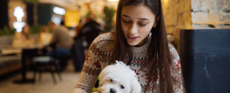 Une belle femme tient son chien, boit un café et sourit dans un café. Top 10 des restaurants pet friendly en france