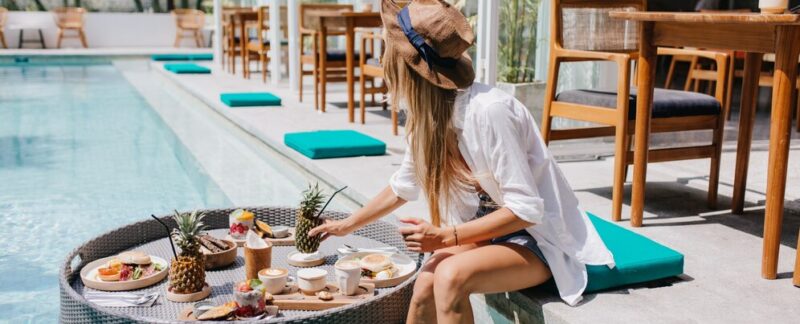 Femme mince portant un élégant chapeau marron mangeant des fruits juteux dans un café de villégiature. hôtels avec piscine chauffée en France
